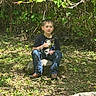 child, boy, kitten, animal, pet, outdoor, nature, leafy, rock, sunlight, shadows, greenery, casual_clothing, jeans, tshirt, sitting, young, peaceful, daylight, forest_floor