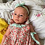 baby, infant, girl, floral_dress, headband, bow, bed, quilt, blanket, soft_lighting, indoors, peaceful, portrait, cute, child, young, sleepwear, hand, face, blue_eyes
