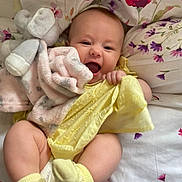 Esmé-Ivy joined the competition — help win amazing prizes! baby, infant, smiling, yellow_clothing, plush_toy, blanket, bed, floral_pattern, socks, cute, happy, child, portrait, indoors, soft_toy, fabric, cushion, skin, person, lying_down