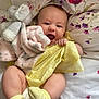 baby, infant, smiling, yellow_clothing, plush_toy, blanket, bed, floral_pattern, socks, cute, happy, child, portrait, indoors, soft_toy, fabric, cushion, skin, person, lying_down