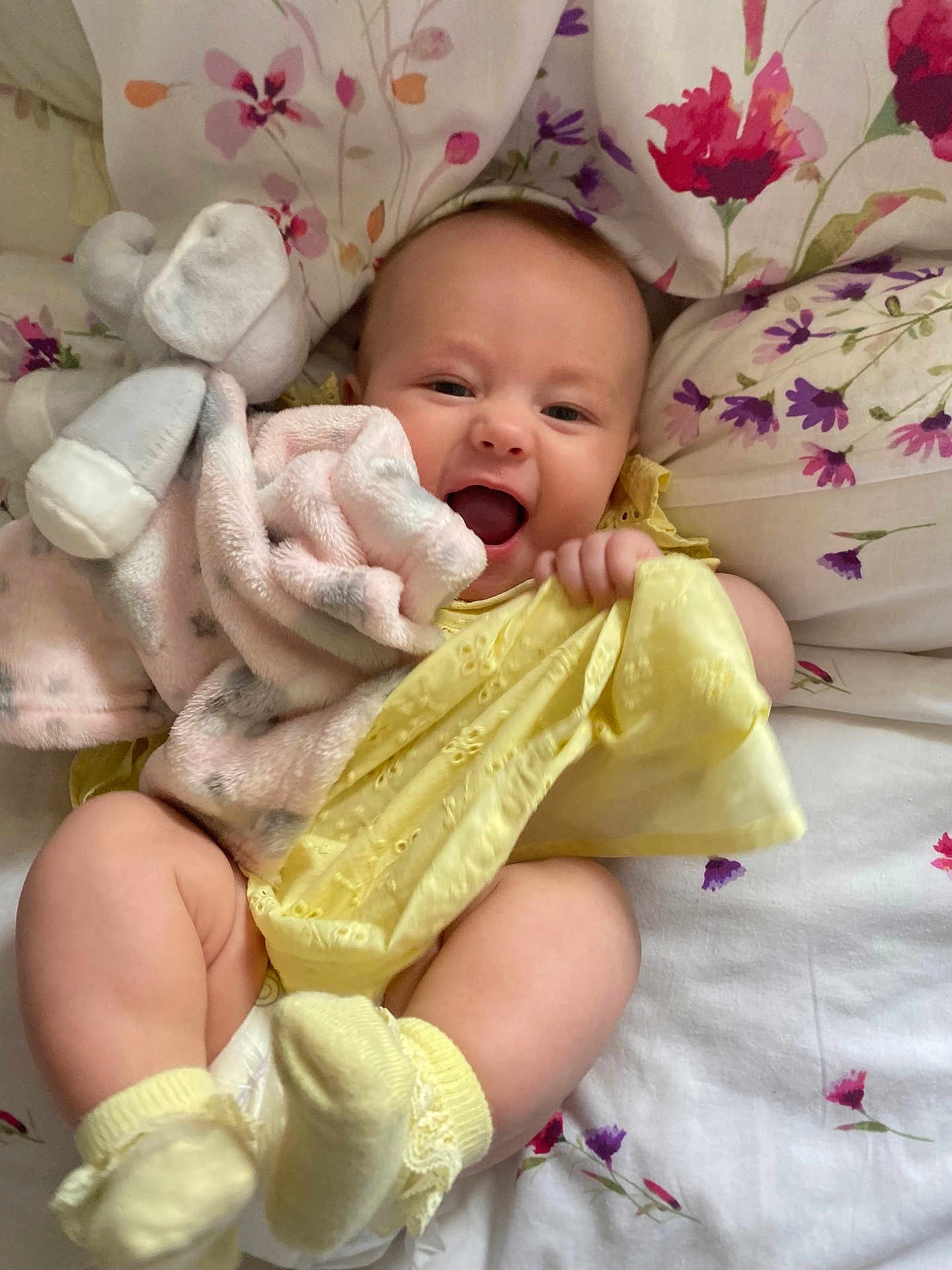 Esmé-Ivy joined the competition — help win amazing prizes! baby, infant, smiling, yellow_clothing, plush_toy, blanket, bed, floral_pattern, socks, cute, happy, child, portrait, indoors, soft_toy, fabric, cushion, skin, person, lying_down