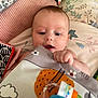 Esmé-Ivy joined the competition — help win amazing prizes! baby, infant, face, hand, blanket, pillow, toy, soft_toy, bed, fabric, pattern, colorful, curious, lying_down, indoors, child, skin, expression, young, person