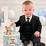 baby, child, toddler, birthday, cake, teddy_bear, suit, tie, black_clothing, portrait, sitting, smiling, balloons, number_one, indoor, celebration, party, decorations, photography, happy_birthday