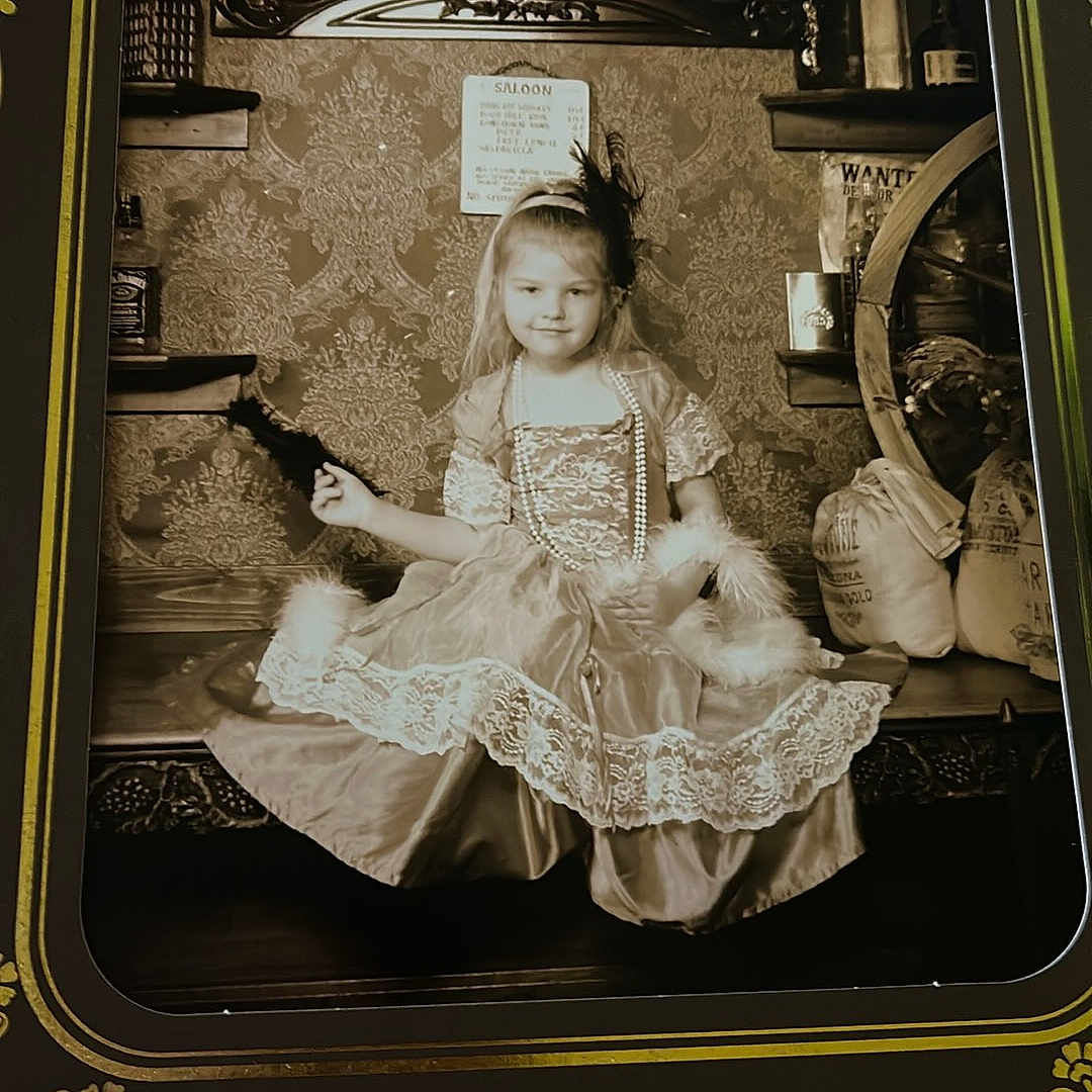 Aimelya is registered to the contest to win money with this photo: antique, beads, bench, child, costume, decor, dress, feather, girl, headband, indoor, old_fashioned, photo_frame, portrait, props, sepia, sitting, smile, vintage, wallpaper