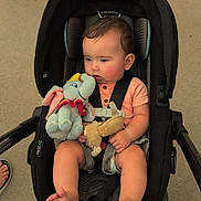 Logan is registered to the contest to win money with this photo: baby, car_seat, plush_toy, dumbo, infant, child, outdoor, concrete, feet, legs, clothing, seatbelt, cute, sitting, black_car_seat, toy, person, footwear, casual, portrait