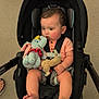 baby, car_seat, plush_toy, dumbo, infant, child, outdoor, concrete, feet, legs, clothing, seatbelt, cute, sitting, black_car_seat, toy, person, footwear, casual, portrait