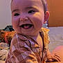 Logan is registered to the contest to win money with this photo: baby, child, smiling, tongue_out, indoor, shirt, patterned_clothing, blanket, bedroom, string_lights, happy, cute, infant, person, portrait, face, hand, soft_lighting, toy, cozy