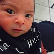 Edgar is registered to the contest to win money with this photo: baby, infant, face, closeup, curious, expression, clothing, text, indoor, person, child, head, skin, eyes, portrait, young, cute, tiled_floor, sleeve, black_garment