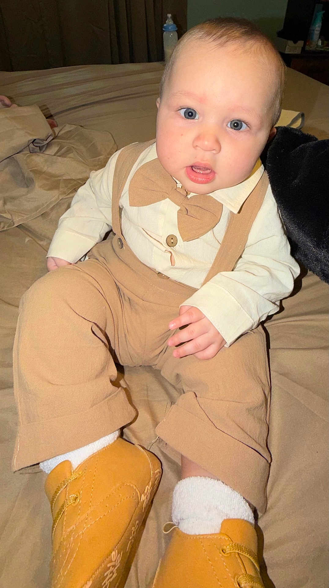 Ayce is registered to the contest to win money with this photo: baby, child, toddler, face, blue_eyes, bow_tie, suspenders, shirt, pants, boots, socks, bed, blanket, indoor, curious, cute, fashion, portrait, person, young