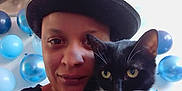 Bellatrix joined the competition — help win amazing prizes! person, cat, black_cat, top_hat, balloons, birthday_badge, indoor, face, celebration, string_lights, whiskers, black_clothing, green_eyes, portrait, holding, decorations, festive, close_up, couch, happy