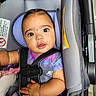 baby, infant, child, car_seat, seatbelt, harness, portrait, wide_eyed, looking_at_camera, indoors, vehicle, safety_seat, purple_clothing, blue_clothing, short_hair, smiling, bottle, toy, close_up, photography