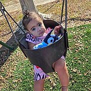Victoria is registered to the contest to win money with this photo: baby, child, toddler, swing, playground, stuffed_toy, outdoor, park, sitting, face, eyes, hair, smiling, clothing, pink_outfit, tree, leaves, grass, fence, daylight