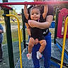 baby, child, parent, playground, outdoor, play_equipment, swing_set, climbing, hanging, smiling, portrait, family, sunlight, park, grass, colorful, infant, casual_clothing, shoes, playtime