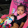 Victoria is registered to the contest to win money with this photo: baby, infant, child, car_seat, car_interior, sitting, portrait, face, eyes, curious, serious_expression, pink, butterflies, toy, stuffed_animal, sheep, bib, clothing, safety_harness, indoor