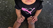 Victoria is registered to the contest to win money with this photo: baby, child, toddler, portrait, sitting, outdoor, pavement, curly_hair, topknot, serious_expression, face, eyes, black_shirt, graphic_shirt, pink_design, shorts, sneakers, flower_shoes, fashion, photography