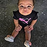 baby, child, toddler, portrait, sitting, outdoor, pavement, curly_hair, topknot, serious_expression, face, eyes, black_shirt, graphic_shirt, pink_design, shorts, sneakers, flower_shoes, fashion, photography