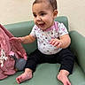 baby, child, infant, smiling, happy, sitting, portrait, face, hands, feet, floral_clothing, black_pants, earring, hair, chair, indoor, pink_bag, toy, green_seat, cute