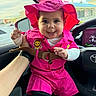 Penelope is registered to the contest to win money with this photo: baby, child, pink_clothing, hat, smiling, car_interior, seat, hand, window, daylight, person, cute, joyful, portrait, apparel, headwear, infant, holding, bright_colors, vehicle