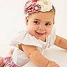 accessory, baby, child, cute, earrings, flower, girl, happy, headband, indoor, jewelry, one_person, pink_skirt, playful, portrait, sitting, smile, white_background, white_top, young_child