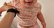 Penelope is registered to the contest to win money with this photo: baby, child, infant, smiling, happy, portrait, floral_shirt, pink_pants, standing, indoor, nursery, changing_mat, adult_hand, wristwatch, face, eyes, open_mouth, home, patterned_background, candid_photo