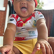 Sean Jr is registered to the contest to win money with this photo: baby, child, smiling, happy, headband, nike, shirt, yellow_shorts, hands, face, portrait, sitting, outdoor, blurred_background, closeup, infant, cute, joyful, apparel, person