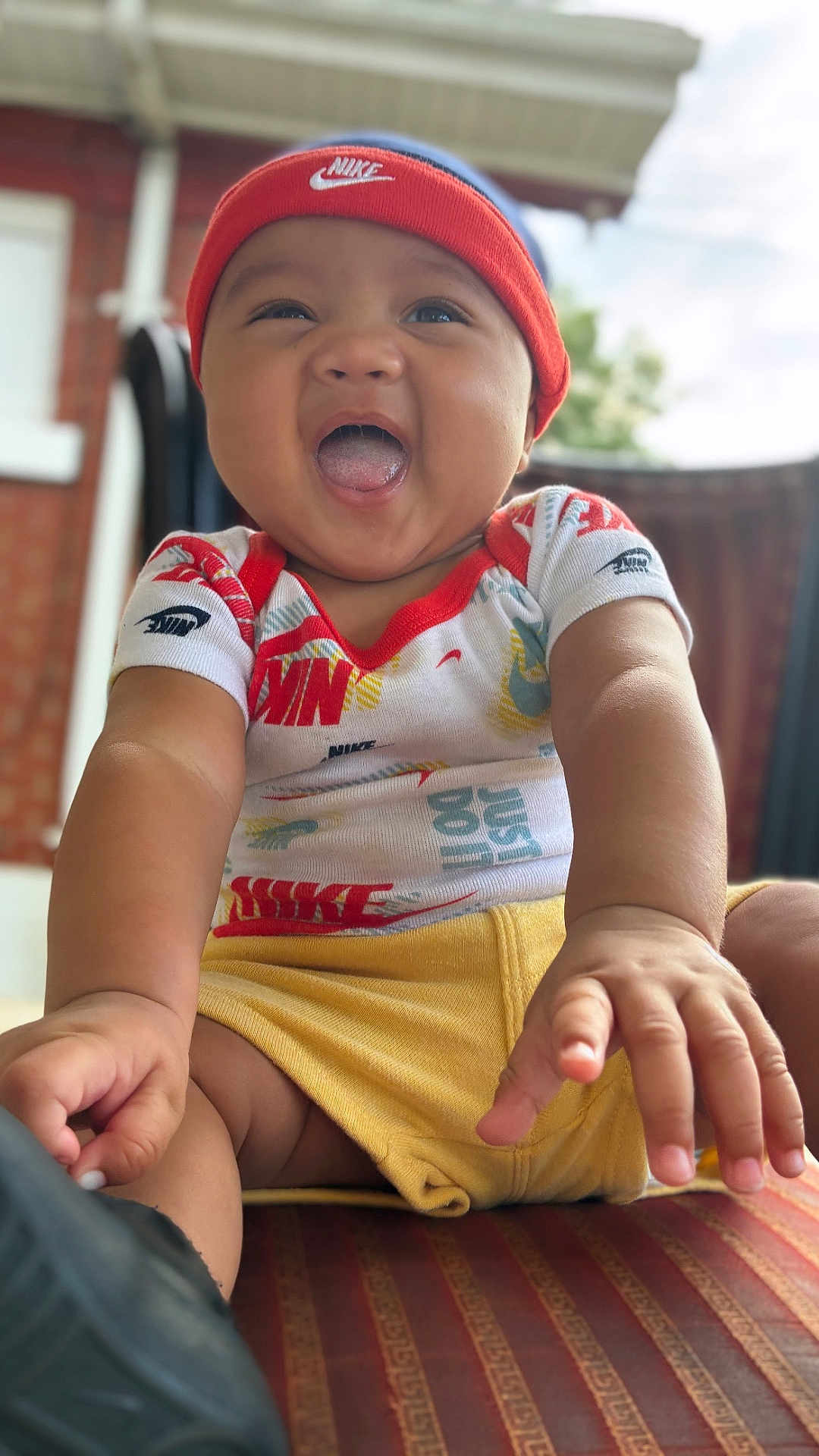 Sean Jr is registered to the contest to win money with this photo: baby, child, smiling, happy, headband, nike, shirt, yellow_shorts, hands, face, portrait, sitting, outdoor, blurred_background, closeup, infant, cute, joyful, apparel, person