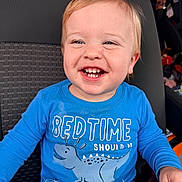 Mason is registered to the contest to win money with this photo: toddler, child, smile, blue_shirt, dinosaur, car_seat, happy, face, teeth, clothing, messy, seat, person, cute, young_child, indoor, portrait, baby, joyful, casual