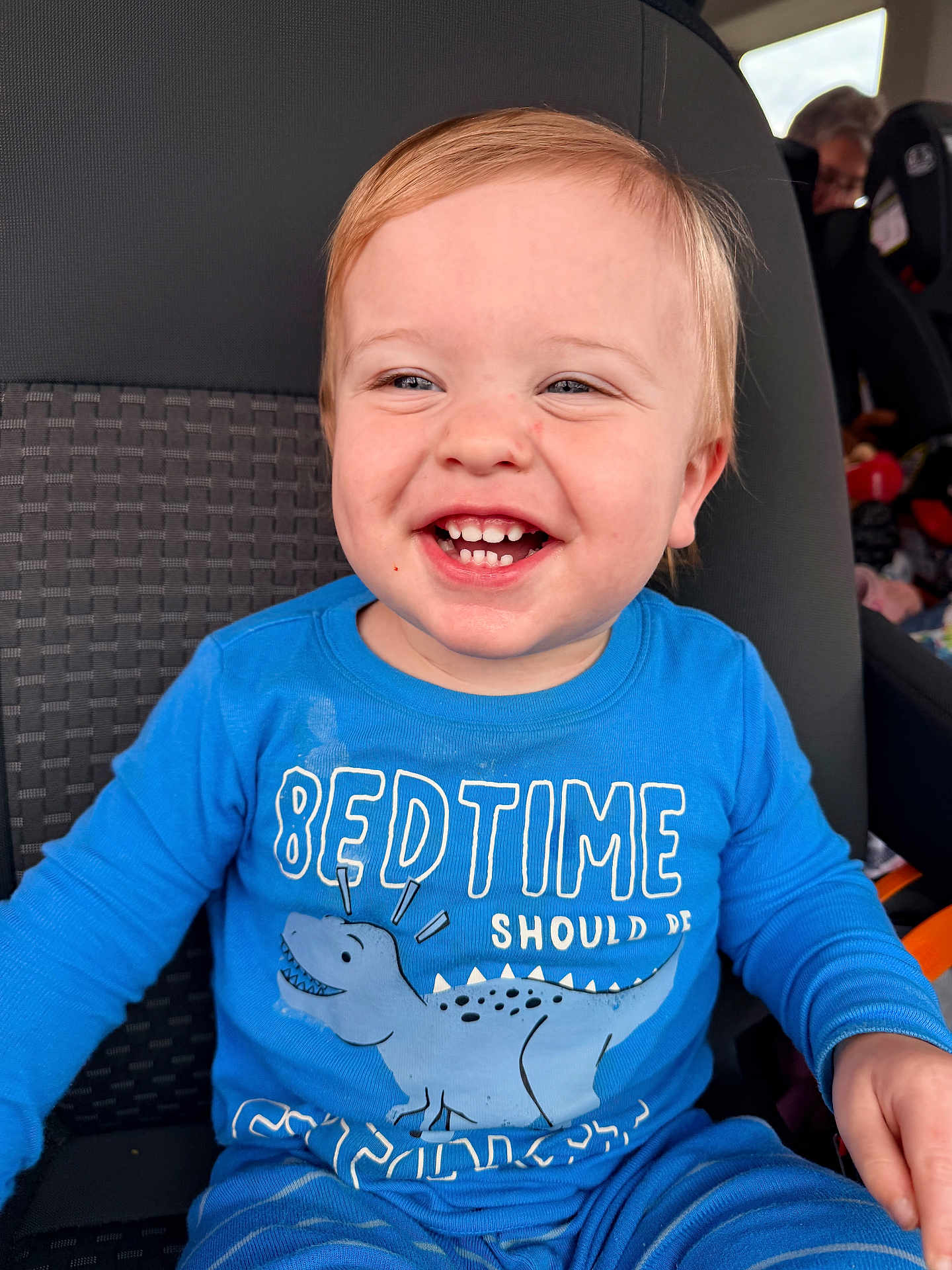 Mason is registered to the contest to win money with this photo: toddler, child, smile, blue_shirt, dinosaur, car_seat, happy, face, teeth, clothing, messy, seat, person, cute, young_child, indoor, portrait, baby, joyful, casual