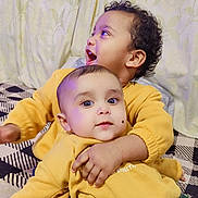 Arsalan joined the competition — help win amazing prizes! toddler, baby, child, yellow_sweatshirt, hugging, indoor, bedspread, patterned, curly_hair, mole, happy, cute, portrait, smiling, clothing, fabric, person, sitting, bedroom, curtain