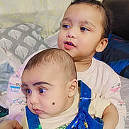 Arsalan joined the competition — help win amazing prizes! baby, toddler, child, holding, face, clothing, overalls, mole, curly_hair, pillow, bed, blanket, indoor, portrait, sitting, cute, expression, person, family, home