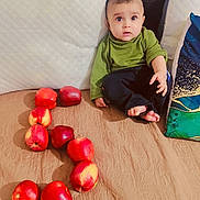 Azlaan joined the competition — help win amazing prizes! apples, baby, bed, black_pants, child, couch, curious, cute, fabric, face, foot, fruit, green_shirt, hand, home, indoor, pillow, red, sitting, soft_lighting