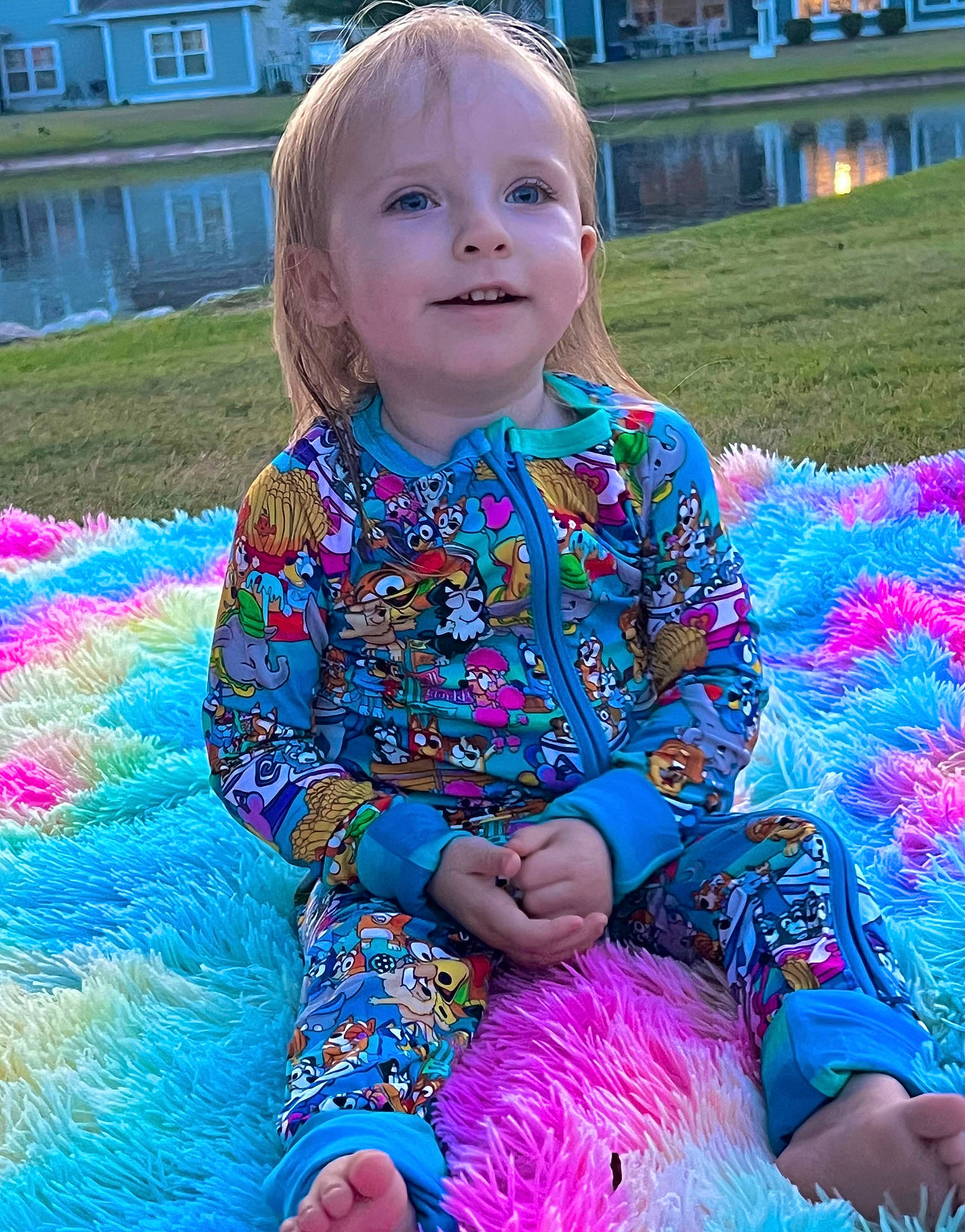barefoot, blanket, blue_eyes, child, colorful_clothing, cute, evening, fluffy, grass, happy, long_hair, nature, onesie, outdoor, pond, rainbow, sitting, smiling, toddler, water