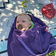 Klara a rejoint le concours — aidez-le/la à gagner de superbes lots ! baby, blanket, calm, child, clothing, face, grass, green, infant, mat, outdoor, pacifier, pattern, purple, relaxing, shadow, striped, sunlight, towel, wrapped