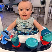 Jayden is registered to the contest to win money with this photo: baby, child, infant, walker, toy, dinosaur, tank_top, indoor, floor_tiles, chair, living_room, person, face, happy, playtime, furniture, home, smiling, cute, seated