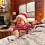 Jayden joined the competition — help win amazing prizes! blanket, cheerful, child, couch, cozy, decor, fireplace, furniture, hat, holiday, indoors, living_room, person, santa_hat, smiling, striped_sweater, table, toddler, window, wooden_cabin