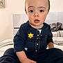Jayden joined the competition — help win amazing prizes! baby, badge, bed, bedding, blanket, child, curious_expression, eyes, face, hand, indoor, legs, mouth, onesie, pajamas, police_costume, portrait, sitting, sock, toddler