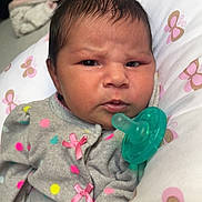 Rhaenyra is registered to the contest to win money with this photo: baby, infant, pacifier, polka_dot, pink_bows, gray_outfit, butterfly_pattern, pillow, close_up, indoor, child, cute, serious_expression, newborn, soft_fabric, cozy, portrait, human, face, skin