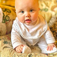 Marcie is registered to the contest to win money with this photo: baby, infant, child, face, blue_eyes, pajamas, bib, cushion, patterned_fabric, indoor, cute, smiling, hands, sitting, soft_lighting, close_up, portrait, plush, cozy, curious