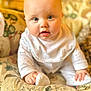 baby, infant, child, face, blue_eyes, pajamas, bib, cushion, patterned_fabric, indoor, cute, smiling, hands, sitting, soft_lighting, close_up, portrait, plush, cozy, curious
