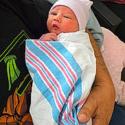 Aurora is registered to the contest to win money with this photo: baby, newborn, infant, swaddle, hospital_blanket, beanie, hat, adult_hand, holding, portrait, indoor, cute, blanket, hospital_room, backpack, tshirt, hand, seat, gaze, person