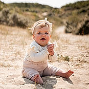 Lou a rejoint le concours — aidez-le/la à gagner de superbes lots ! baby, child, sand, beach, sitting, headband, clapping, smiling, sunlight, nature, outdoor, dunes, grass, cute, infant, happy, portrait, clothing, feet, hands