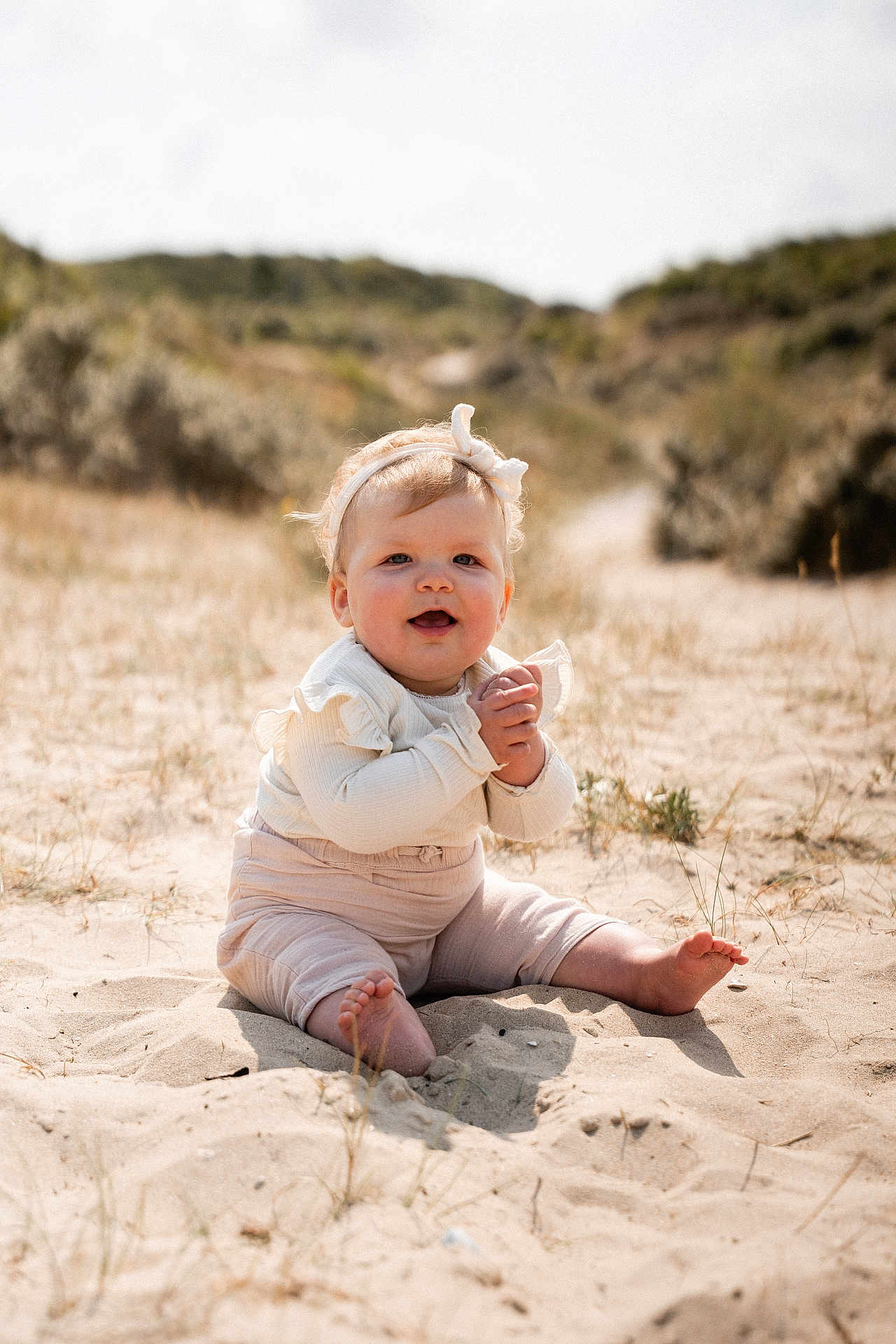 Lou a rejoint le concours — aidez-le/la à gagner de superbes lots ! baby, child, sand, beach, sitting, headband, clapping, smiling, sunlight, nature, outdoor, dunes, grass, cute, infant, happy, portrait, clothing, feet, hands