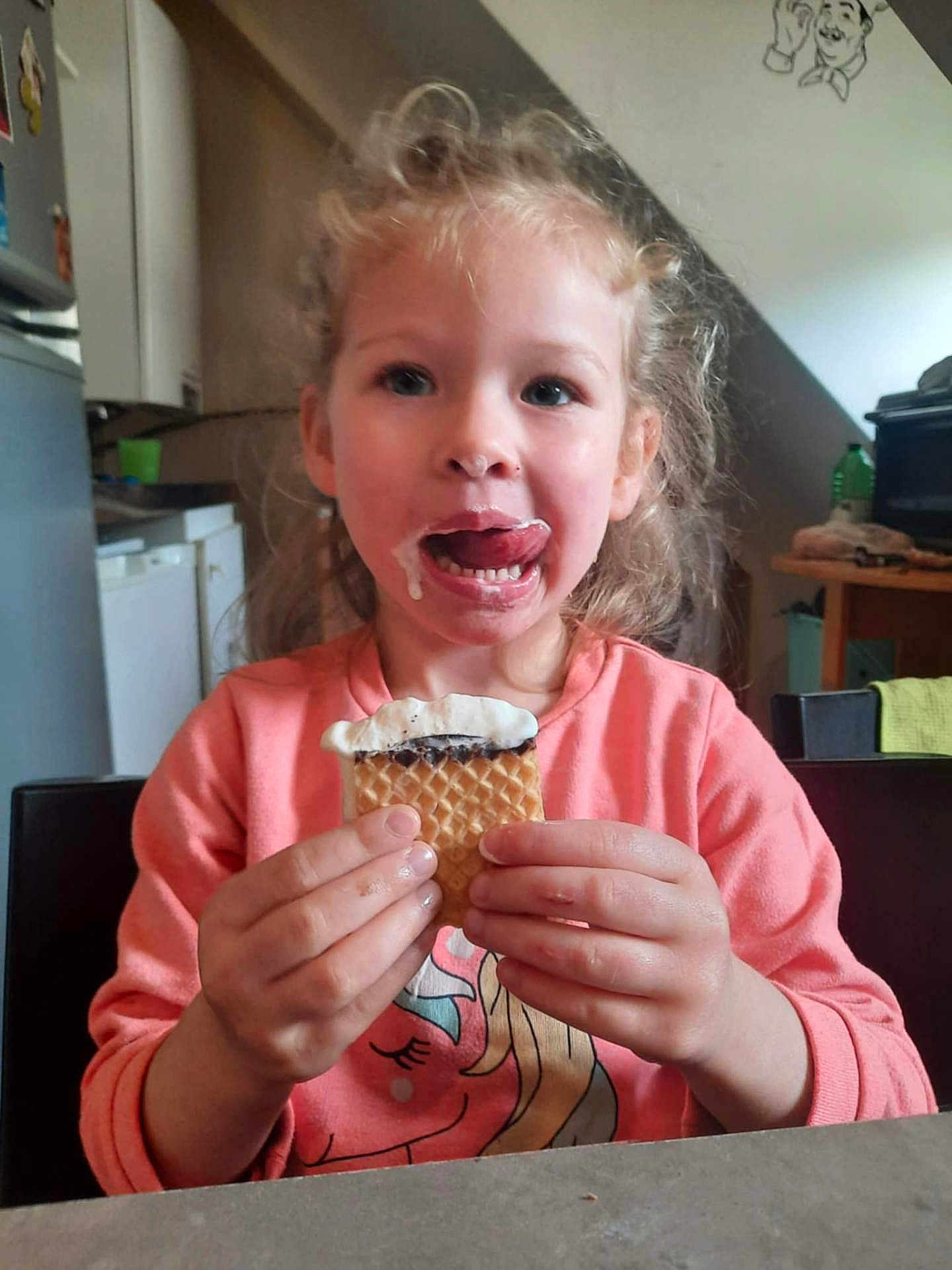 Alana participe au concours pour gagner de l'argent avec cette photo : child, curly_hair, ice_cream, messy_face, pink_shirt, unicorn, kitchen, table, happy, licking, food, snack, person, indoor, smile, cute, young, holding, dessert, playful