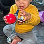 Amir joined the competition — help win amazing prizes! toddler, child, indoor, yellow_sweater, gray_pants, barefoot, red_ball, pacifier, wooden_floor, playpen, toy, cute, baby, sitting, reaching, curly_hair, expression, person, floor, home
