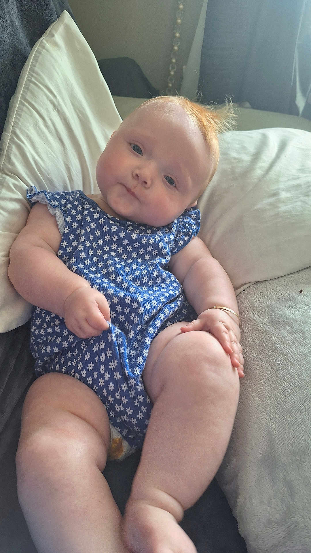 Delilah Denise is registered to the contest to win money with this photo: baby, infant, child, blue_outfit, floral_pattern, pillow, soft_texture, red_hair, curious_expression, indoors, couch, plush, skin, legs, arms, hand, cute, chubby, portrait, relaxed