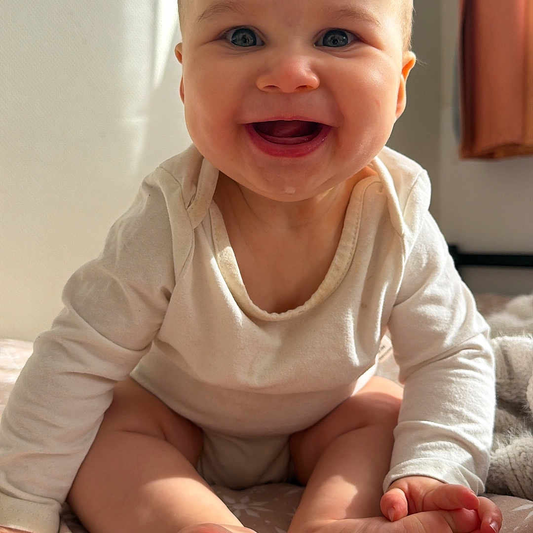 Esaïe participe au concours pour gagner de l'argent avec cette photo : baby, child, smiling, happy, sitting, blue_eyes, infant, cute, indoor, bedspread, white_clothing, sunlight, portrait, toes, hands, curtain, skin, cozy, young, face
