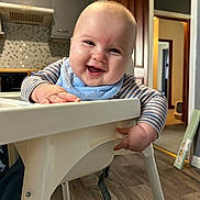 Lewis joined the competition — help win amazing prizes! baby, high_chair, smiling, indoor, kitchen, bib, striped_clothing, happy, child, person, furniture, wood_floor, cabinet, doorway, face, hand, cute, infant, home, portrait