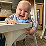 baby, high_chair, smiling, indoor, kitchen, bib, striped_clothing, happy, child, person, furniture, wood_floor, cabinet, doorway, face, hand, cute, infant, home, portrait