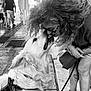 dog, woman, curly_hair, glasses, sidewalk, urban, leash, love, affection, pet, street, tattoo, sneakers, black_and_white, close_up, outdoor, interaction, happy, canine, people