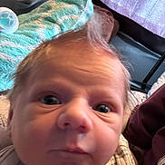 Andrew is registered to the contest to win money with this photo: baby, newborn, infant, face, eyes, nose, mouth, hair_tuft, onesie, button, pacifier, blanket, pillow, bedding, close_up, portrait, indoors, soft_texture, curious_expression, person